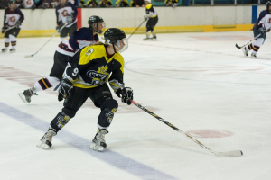 Menschen spielen Schnee-Eishockey mit Stöcken und Helmen, mit anderen und einer Wand im Hintergrund.