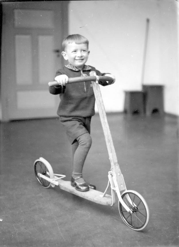Junger Junge, der ein Motorrad mit einem Lächeln fährt, vor einer Tür und einer Wand, Schwarz-Weiß-Foto.