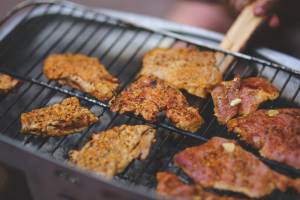 Person grillt Fleisch auf einem Grill mit Hilfe von Grillzangen, mit einem leicht unscharfen Hintergrund.