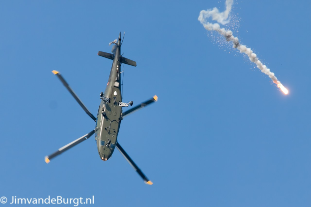 Militärhubschrauber steigt mit einer rauchenden und Feuer speienden Rakete auf, Text in der unteren linken Ecke.