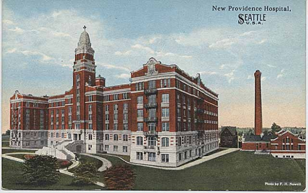 Postkarte des New Providence Hospital in Seattle, Washington, zeigt ein großes Gebäude mit Fenstern, umgeben von Bäumen, Pflanzen, Gras, einem Weg, einem Turm im Hintergrund und einem bewölkten Himmel, mit Text auf der Postkarte.