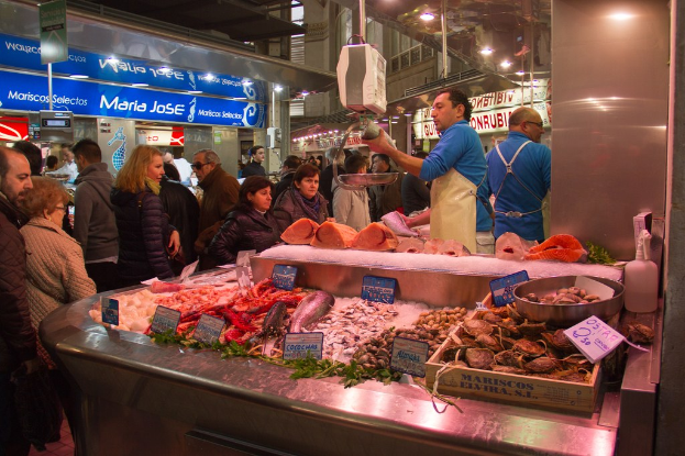 Marktszene mit Menschen, die gehen, einige Fisch auf Brettern in der Mitte schneiden, Fisch unten und Geschäfte, Bretter, Pfähle und Lichter im Hintergrund.