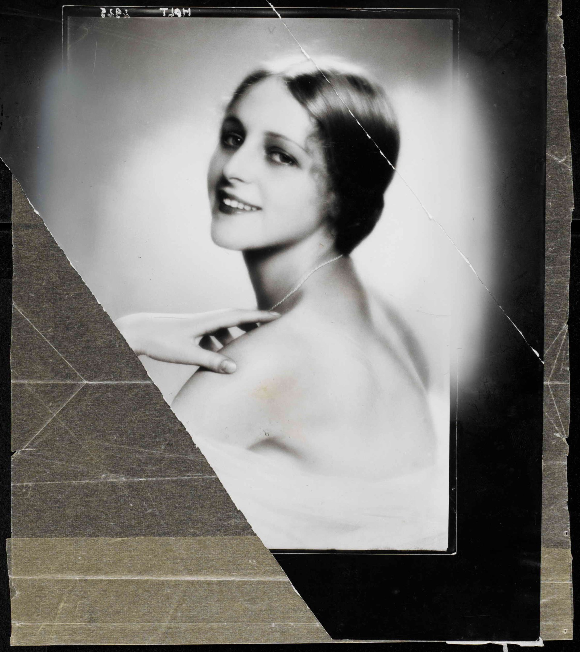 Schwarzes und weißes Foto einer Frau in einem Kleid mit 1920er-Jahre-Frisur in einem ordentlichen Dutt, die direkt in die Kamera lächelt.