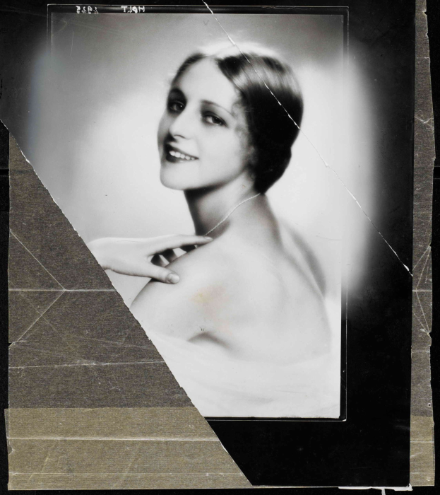 Schwarzes und weißes Foto einer Frau in einem Kleid mit 1920er-Jahre-Frisur in einem ordentlichen Dutt, die direkt in die Kamera lächelt.