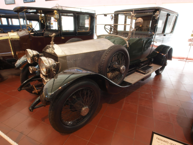 Ein klassisches Auto mit glänzendem Lack und klassischem Design, das in einem Museum ausgestellt ist, von einem Seil abgesperrt und von Informationsschildern und gerahmten Ausstellungen umgeben ist.