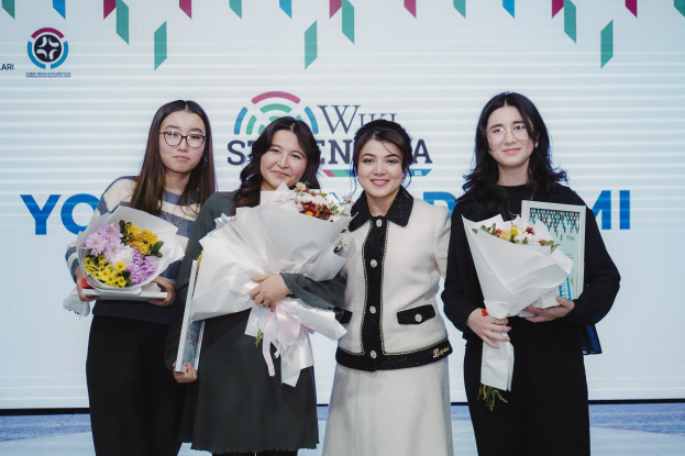 Vier Frauen, die zusammenstehen und Blumensträuße halten, mit einem Banner im Hintergrund, auf dem "Yoyogi International Women's Day" steht