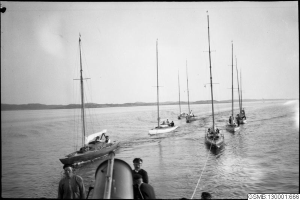 Ein Schwarz-Weiß-Foto von mehreren Segelbooten, die im Wasser rasen, mit Menschen an Bord, vor einem Hintergrund aus Hügeln und einem klaren Himmel, und einem Text unten, der "Segelbootrennen in San Francisco, Kalifornien" lautet.