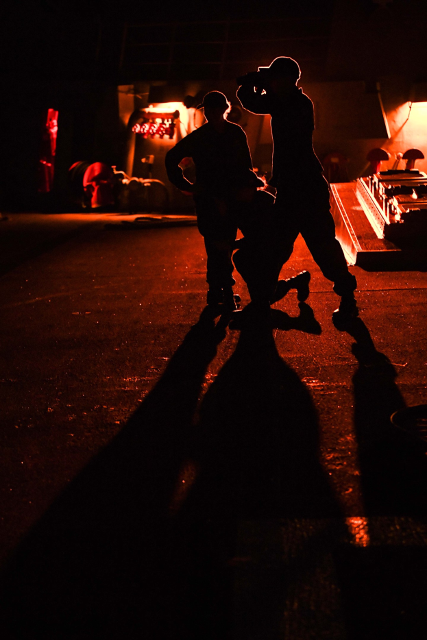 Zwei Männer auf einer Bühne bei Nacht, die Schuhe tragend und von Hintergrundlichtern beleuchtet.