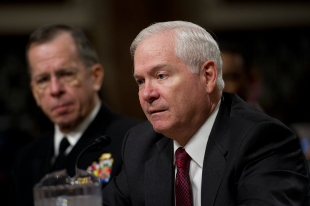 Zwei Männer in Anzügen und Krawatten sitzen an einem Tisch mit einem Mikrofon und einem Glasgefäß, mit einem unscharfen Hintergrund.