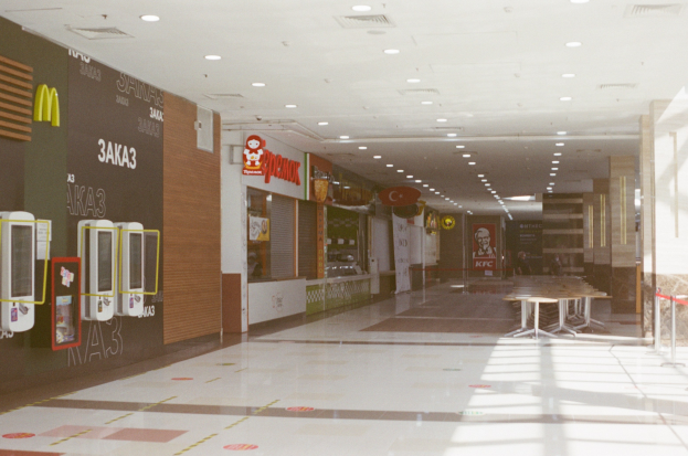 Inneneinrichtung eines Fast-Food-Restaurants mit Tischen, Stühlen, einer Wandmontage, Maschinen, Deckenbeleuchtung und einer Glaswand auf der rechten Seite.