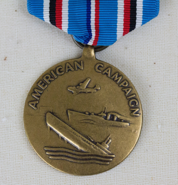 Goldmedaille mit einer roten, weißen und blauen Schleife, die mit 'American Campaign' beschriftet ist, auf einer weißen Oberfläche liegend.