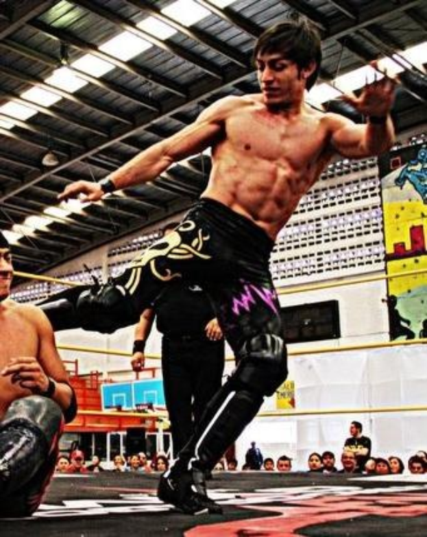 Zwei Wrestler in einem Ring mit ausgestreckten Armen, umgeben von einer Menge, mit einer Person im Hintergrund, Tafeln mit Bildern und Text auf der rechten Seite und Beleuchtung von oben.