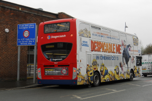 Ein weißer und roter Bus parkt auf einer Straße mit einer roten Backsteinwand und einem blauen Warnschild im Hintergrund.