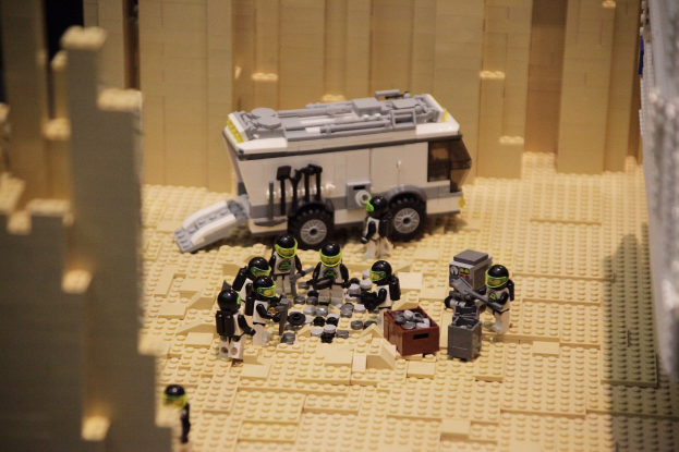 Lego-Modell einer Star-Wars-Szene mit einem Geländefahrzeug im Vordergrund, verstreuten Spielzeugen und einer Wand im Hintergrund.