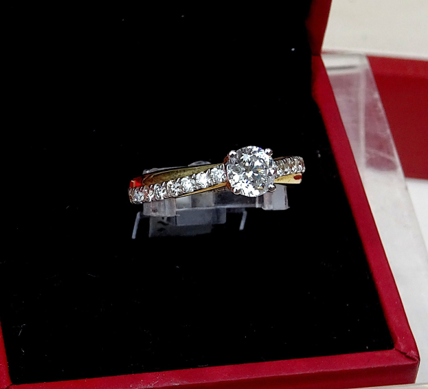 A deep red ring box containing a diamond engagement ring with a halo of smaller diamonds, placed on a table.