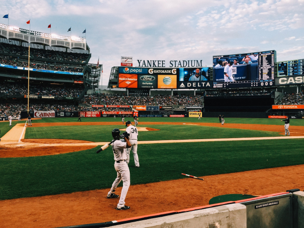 Baseball-Spiel im Gange im Yankee-Stadion mit Spielern auf dem Feld und Zuschauern in den Rängen bei bewölktem Himmel.