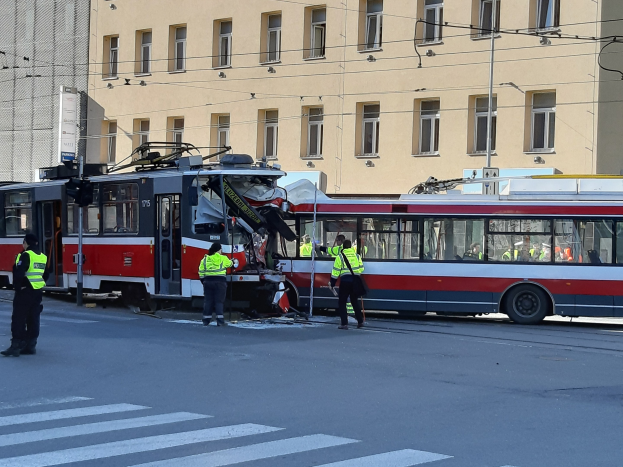 Red and white tram crashed on the side of the road with a few people nearby and a building in the background.