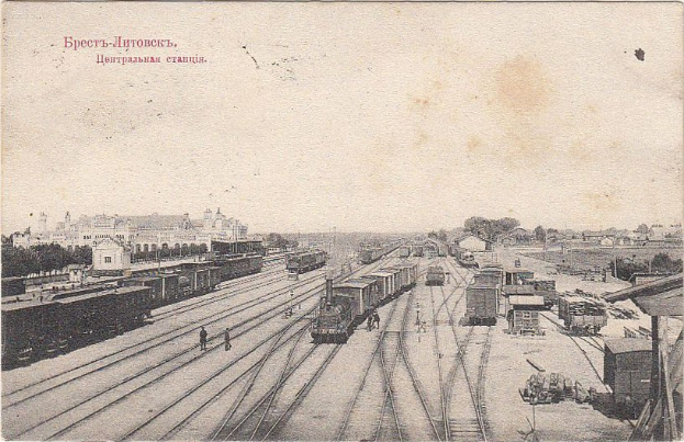 Schwarzes und weißes Foto eines Bahnhofs in Moskau mit Zügen auf den Gleisen, Menschen auf dem Bahnsteig, Gebäuden und Bäumen im Hintergrund und Text oben.