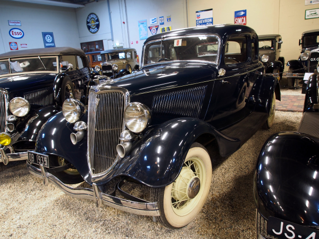 Eine Gruppe von Oldtimern in einer schwach beleuchteten Garage mit einer Wandtafel und Beleuchtung an der Decke.