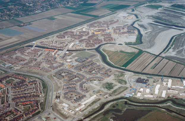 Luftaufnahme einer Stadt mit dichtem Gebäudebestand, Straßen, Feldern, Bäumen und einem zentralen Reservoir, das von städtischen Gebieten umgeben ist.