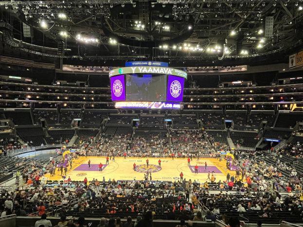 Große Halle mit Zuschauern bei einem Basketballspiel im Staples Center, mit beleuchtetem Spielfeld, umgebenden Sitzplätzen, Geländern und einem großen Überkopfbildschirm.