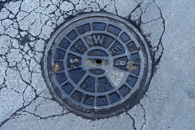 Ein gebrochener Metallschachtdeckel an der Straße mit eingravierter Schrift.