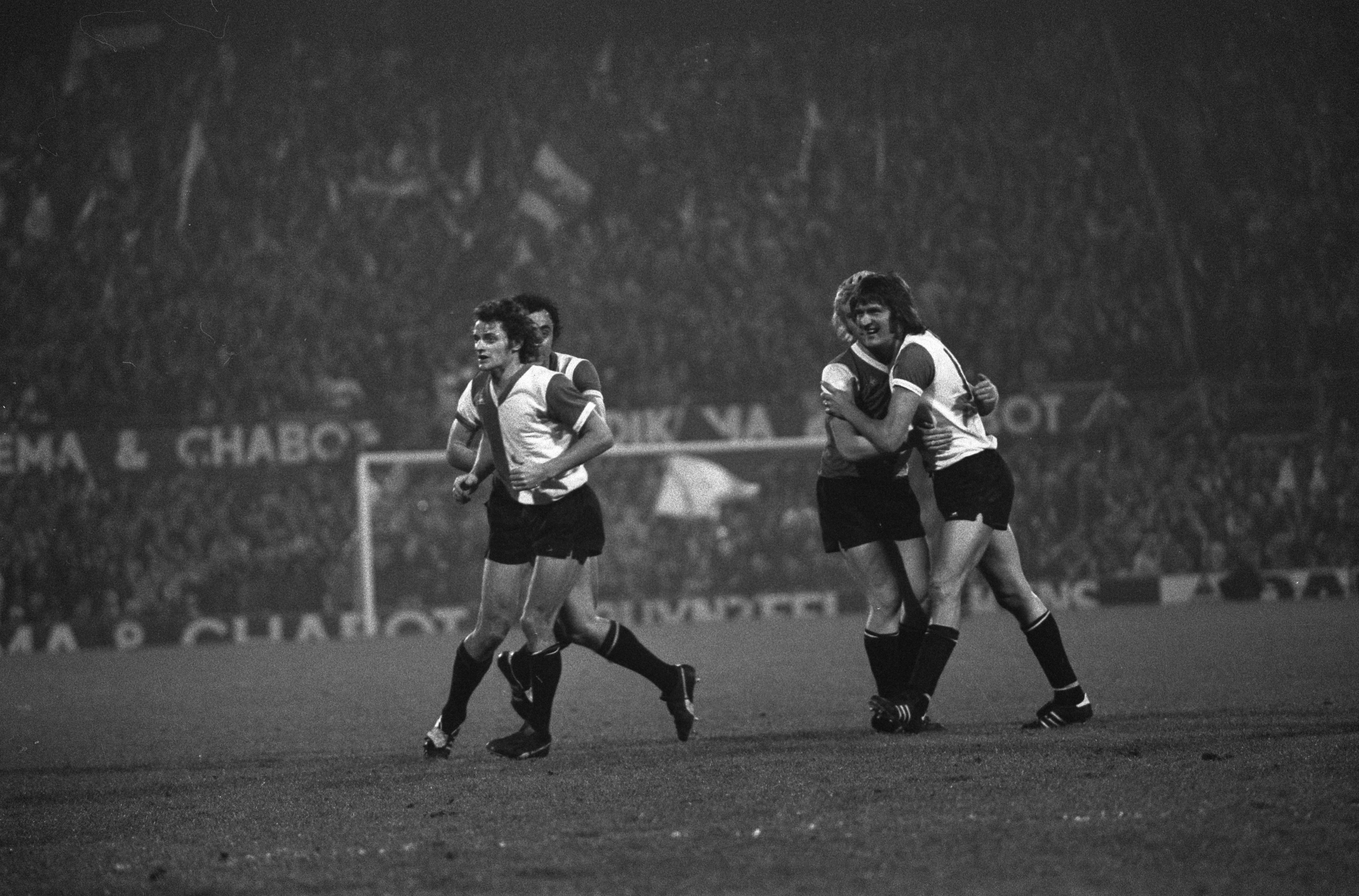 Schwarzes und weißes Foto von Männern, die Rugby auf einem Feld mit einem Netz und Bannern im Hintergrund spielen.