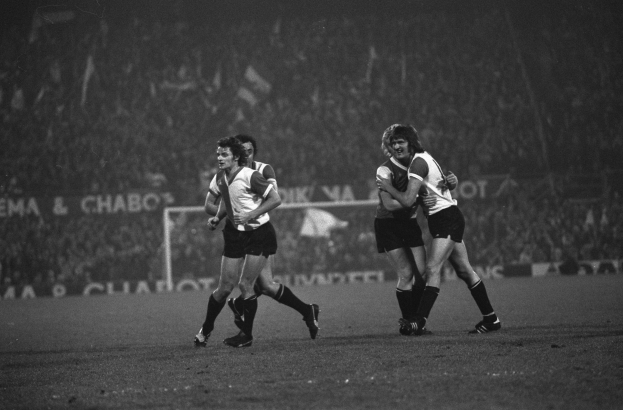 Schwarzes und weißes Foto von Männern, die Rugby auf einem Feld mit einem Netz und Bannern im Hintergrund spielen.