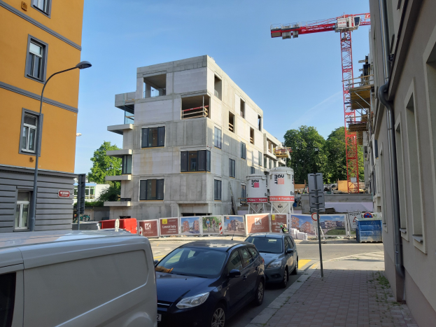 Eine Stadtstraße in Berlin, Deutschland mit parkenden Autos, Gebäuden, Laternen, Schildern, Bäumen und einem Kran im Hintergrund, der den Bau neuer Wohnungen anzeigt.