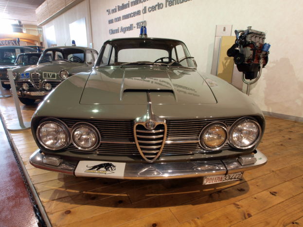 Klassisches 1970er Alfa Romeo Giulietta Sprint GT Junior im Museum mit Seilabsperrungen und Wandtext unter warmer Deckenbeleuchtung ausgestellt.