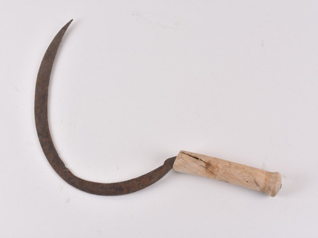 Ein alter rostiger Sichel mit einem Holzgriff auf einer wei\uen Oberfl"ache.