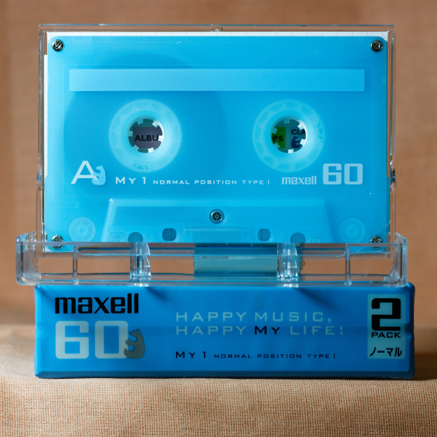 Blaue Kassette mit der Aufschrift "Maxell Happy Music, Happy My Life" auf brauner Oberfläche.