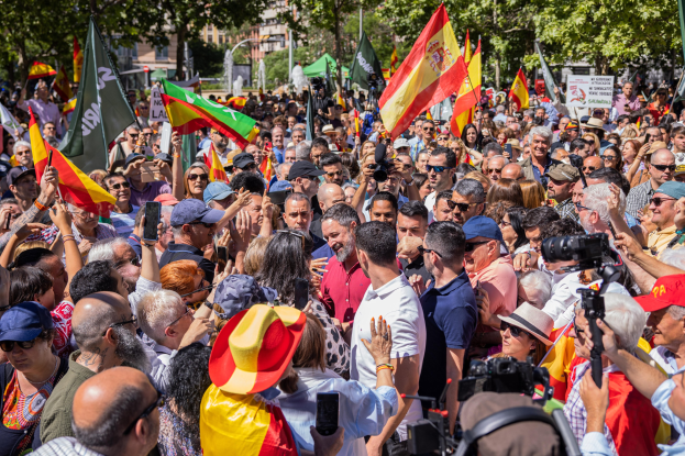 Große Gruppe von Menschen protestiert vor einer Menge in Barcelona, einige halten Fahnen und Mobiltelefone, andere Kameras, mit Bäumen und Gebäuden im Hintergrund.