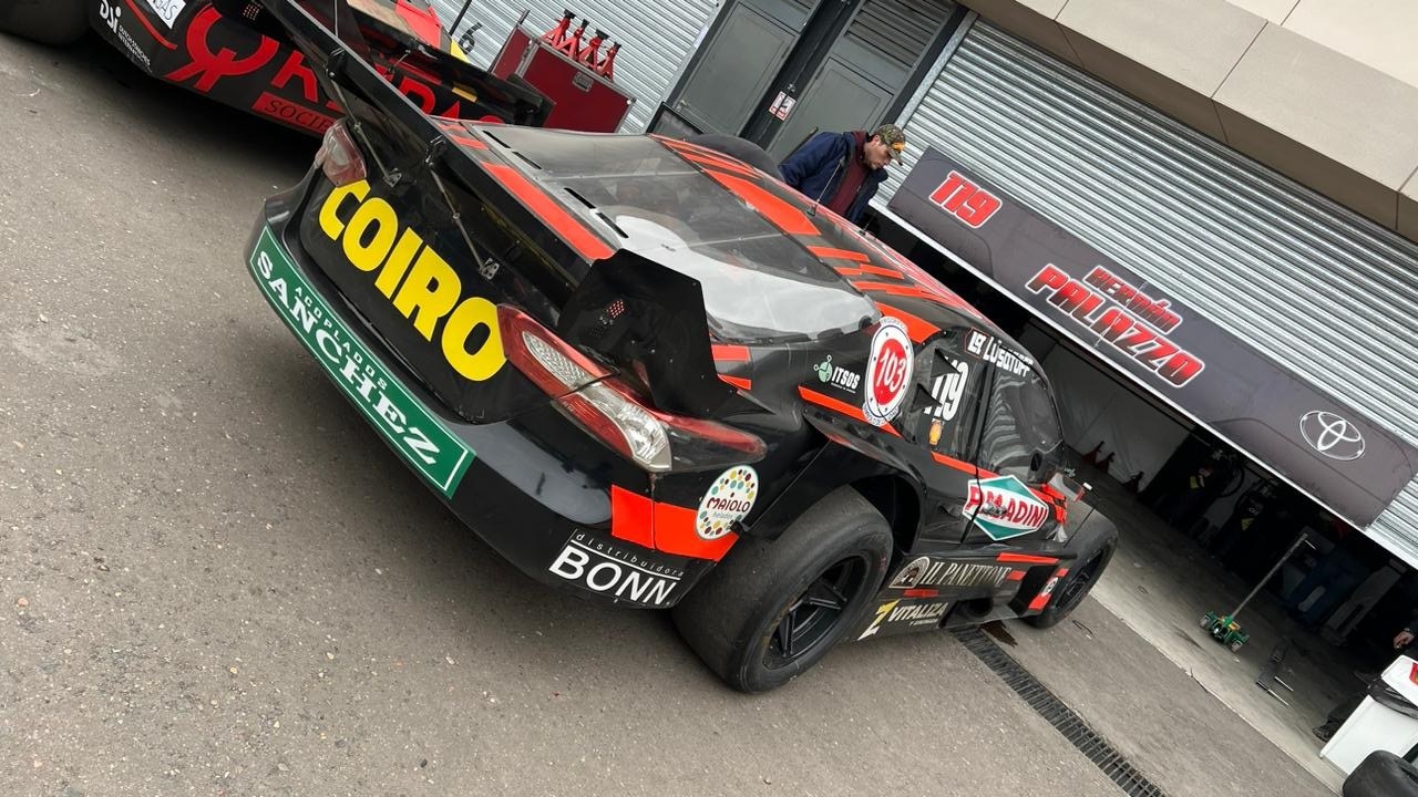 Gruppe von Rennwagen vor einem Gebäude mit "Le Mans 2019"-Banner geparkt, Menschen in der Nähe.