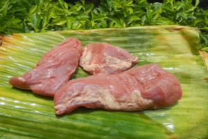 Drei Stücke rohes Huhn auf einem Bananenblatt mit verstreuten grünen Blättern.