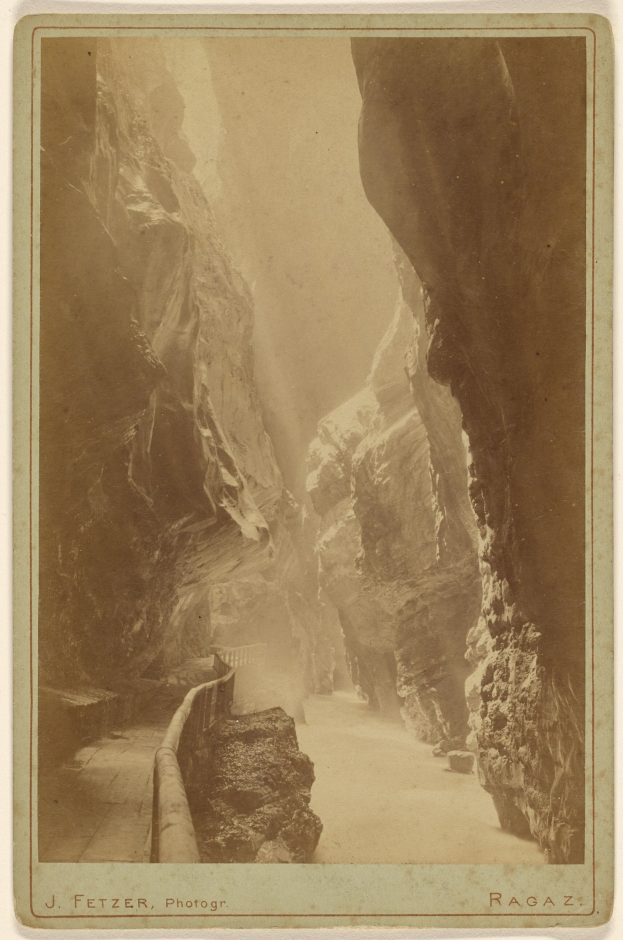 Schwarzes und weißes Foto eines schmalen Canyons mit steinigen Seiten und einem gewundenen Pfad hindurch, mit Text unten.