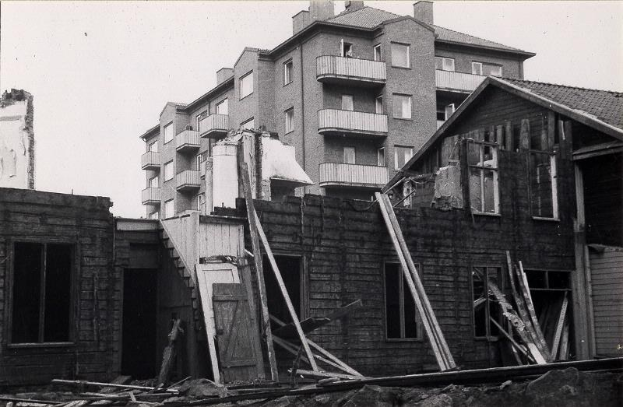 Schwarzes und weißes Foto eines abgerissenen West End Apartments-Gebäudes mit Schutt auf dem Boden und dem Himmel im Hintergrund.