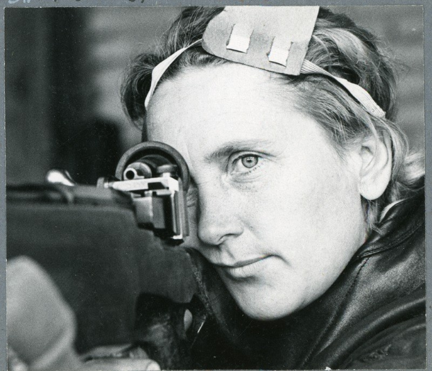 Ein Schwarz-Weiß-Foto einer Frau mit einer Waffe in der Hand, die konzentriert auf ihr Ziel schaut.
