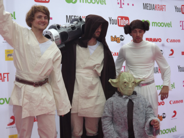 A group of people in Star Wars costumes posing on a red carpet with a banner in the background.