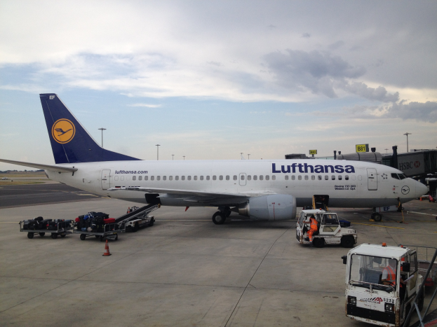 Lufthansa Airbus A320-200 auf dem Rollfeld am Frankfurter Flughafen mit Boden Service Fahrzeugen, Verkehrskegeln und Informationsschildern unter einem bewölkten Himmel.