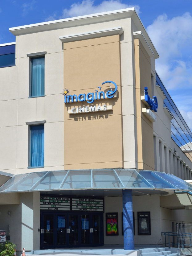 Exterior view of the Imagine Cinemas building in San Diego, California, featuring windows, doors, a signboard, plants, poles, a staircase, railing, and a cloudy sky.