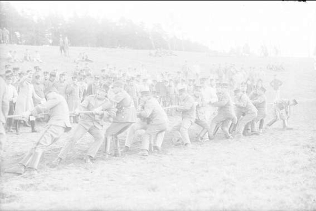 Schwarzes und weißes Bild von Männern, die Baseball in einem Feld spielen, einige halten Schläger, während ein körperlicher Streit unter den Spielern im Vordergrund und Bäume im Hintergrund sichtbar sind.