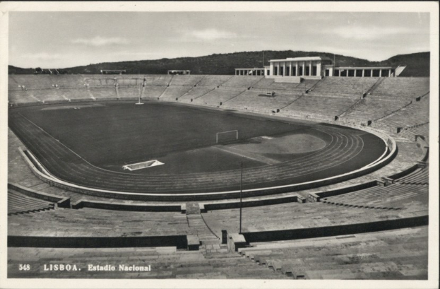 Schwarzes und weißes Foto des Olympiastadions in Lissabon, Portugal, das das Stadion umgeben von Stufen und Pfählen zeigt, mit Hügeln und bewölktem Himmel im Hintergrund und Text unten.