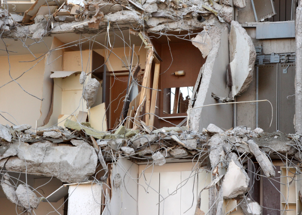 Ein teilweise abgerissener Bau mit zerbrochenen Wänden, verstreuten Trümmern und verstreuten Holz- und anderen Materialstücken auf dem Boden.