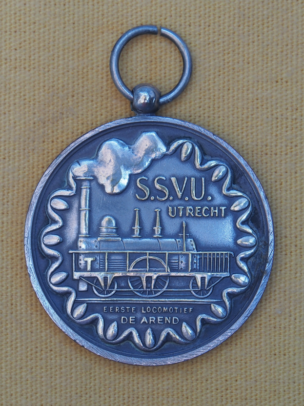 Eine Silbermedaille mit einem Bahn-Design und Text, die auf einem Tuch liegt.