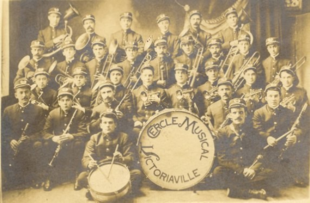 Schwarzes und weißes Foto einer frühen Band, die mit Musikinstrumenten posiert, einschließlich eines Schlagzeugs mit sichtbarem Text in der Mitte.