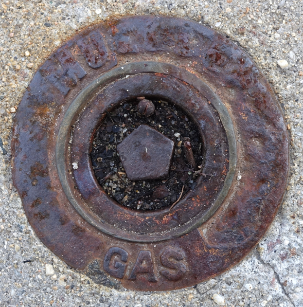 Rostiger Metall-Schachdeckel auf dem Boden mit dem Wort "Gas" darauf.