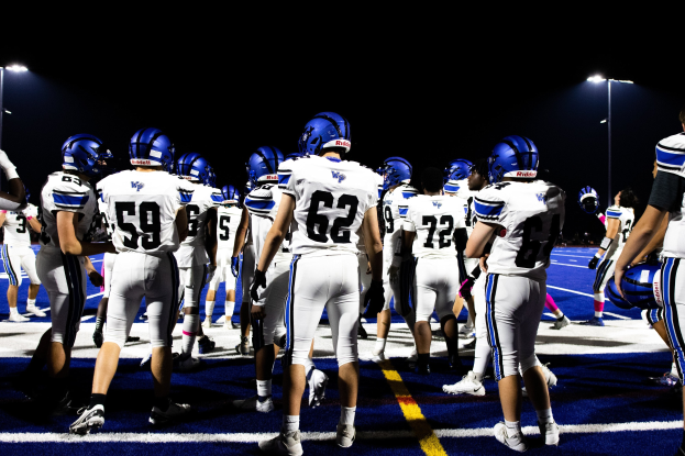 Eine Gruppe von Fußballspielern in Helmen und Stollenschuhen steht auf einem Feld unter Flutlicht und sieht bereit für ein Spiel aus.