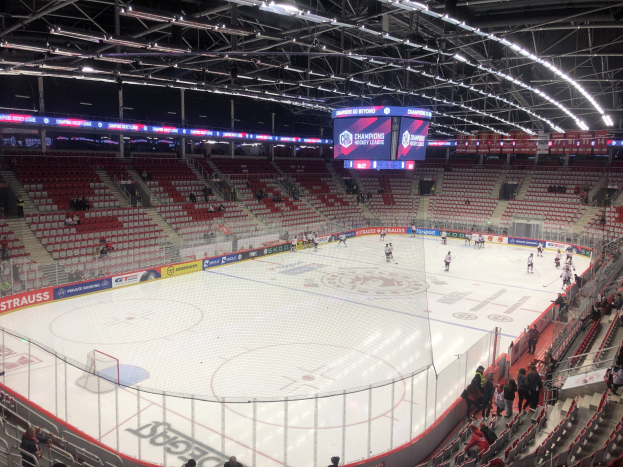 Eishockeyspiel in einer großen Arena zwischen den St. Louis Blues und den Detroit Red Wings, mit Zuschauern auf Sitzen und Stehplätzen in der Nähe der Eisfläche, umgeben von einem Zaun und Metallrahmen, unter einer Decke mit Deckenleuchten und einem Anzeigebildschirm.