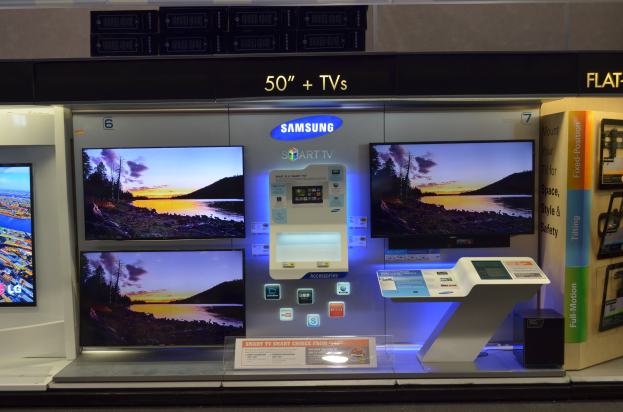 Ladenauslage mit mehreren Fernsehern, darunter ein Samsung Smart TV und ein Flachbildschirmmodell, mit Texttafeln und anderen Gegenständen im Hintergrund.